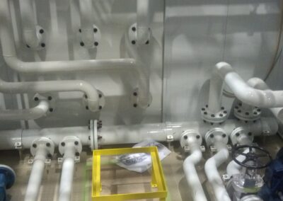Industrial piping manifold with white pipes, flanges, valves and pump motor in a mechanical plant room.