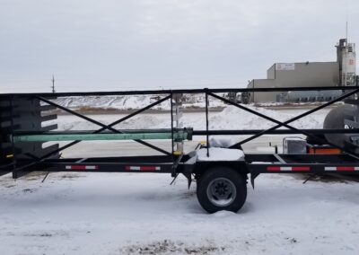 Single-axle cable reel trailer with adjustable spindle, black steel frame on snow, industrial yard backdrop.