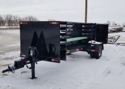 Black heavy-duty livestock stock trailer with slatted sides and front hitch parked on a snowy lot