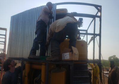 Construction crew installing corrugated metal panels on steel frame around heavy machinery at outdoor industrial jobsite