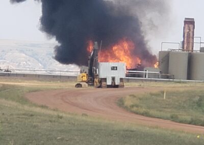 Massive industrial oil facility fire with thick black smoke near storage tanks on rural site, emergency response scene