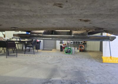 Close-up of welded steel bracket under vehicle chassis in auto repair shop, showing custom fabrication and welds.