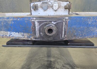 Close-up of welded steel plate with pivot bushing on blue beam, heavy equipment repair fabrication, rusted metal surface