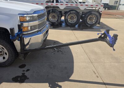 Chevy pickup with front bumper tow bar hitch tied with blue rope, heavy-duty towing setup near tri-axle trailer