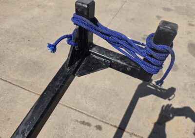Blue braided rope tied between two black metal posts on a trailer hitch, showing secure tie-off knot for cargo.