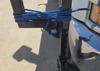 Truck front receiver hitch with black U-bracket, blue rope wrapped around posts to secure cargo.