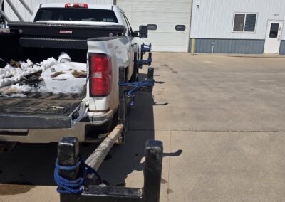 Pickup with custom welded pipe rack and blue tie-downs outside EZ Welding & Fabrication shop with large bay door.