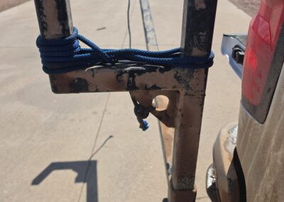 Rusty truck hitch bed extender rack with blue rope, used for hauling lumber or ladders at a jobsite parking lot