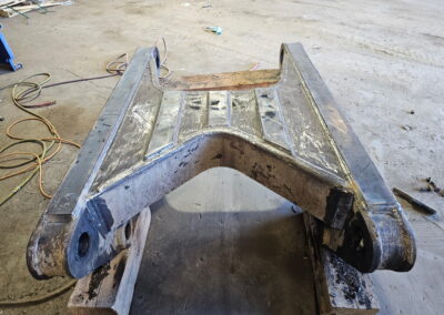 Reinforced excavator boom yoke after welding repair in fabrication shop, heavy equipment steel part on blocks